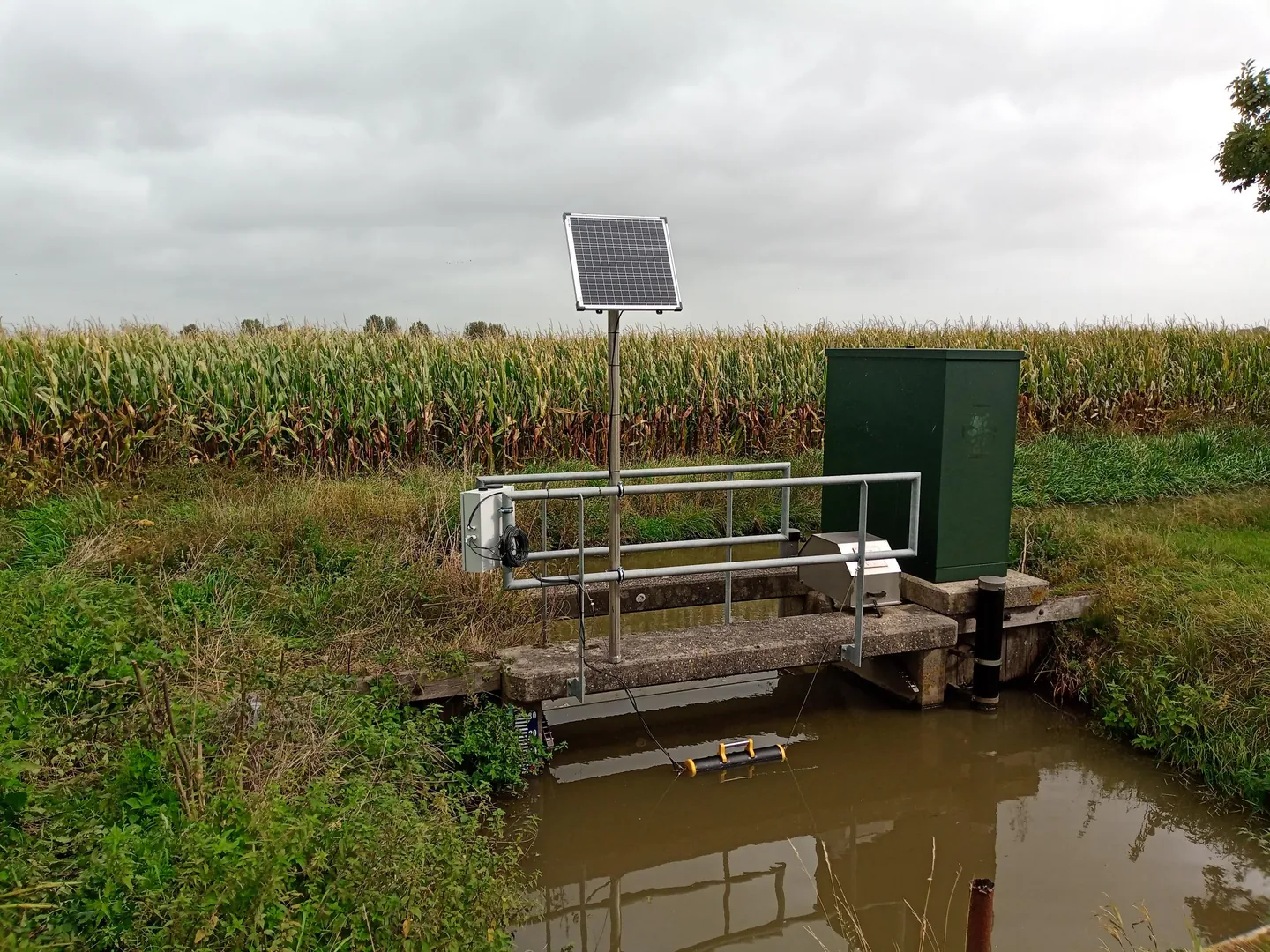 Messstation mit Solarmodul und schwimmender Sensorhalterung an einem Wasserlauf.