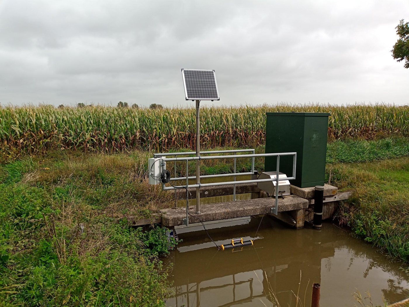 Nitrat-Messstation an einem Wassergraben: Schaltschrank mit Aquatos Web LTX, Solarmodul am Mast und die Sonde im gelb-schwarzen Schwimmer im Wasser
