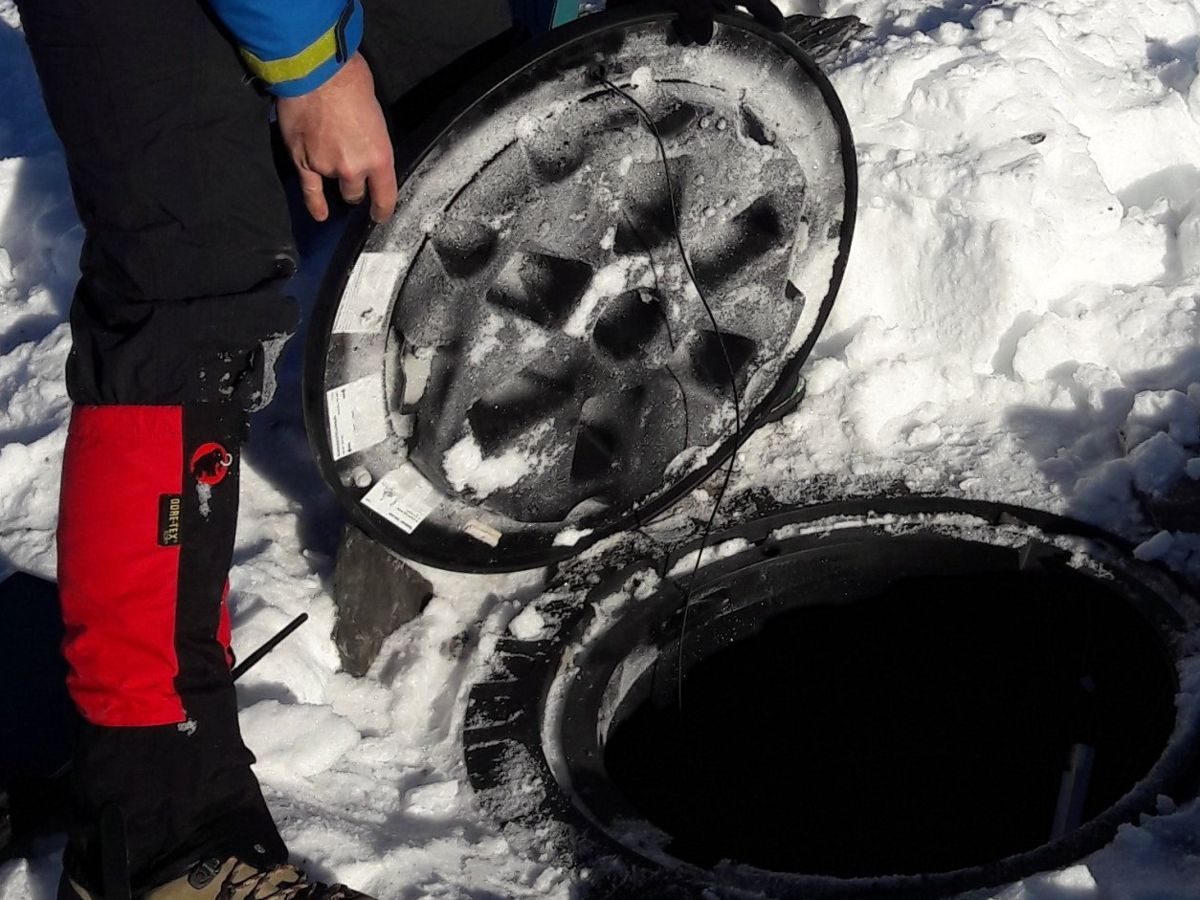 Techniker hebt im Schnee einen Schachtdeckel an, Temperatur-Messkette wird heraus­geführt