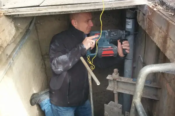 TerraTransfer-Techniker montiert mit der Bohrmaschine eine Halterung im Pegelschacht